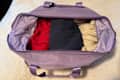 Lavender florence by mills x DELSEY PARIS Weekender Bag  duffel bag filled with a red sweater, dark clothing, and a beige item, resting on a soft surface.