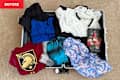 A partially packed suitcase with various clothing items, including t-shirts, a floral wallet, and a blue tank top.