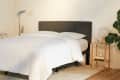 Cozy bedroom with a dark gray upholstered headboard, white bedding, wooden side table, and potted plants.