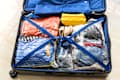 Open suitcase with clothes in vacuum-sealed bags, blue straps, and a yellow pouch.