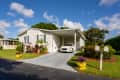 Single-story home with a carport, white car, colorful plants, and a mailbox in a sunny neighborhood.