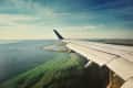 Airplane wing over coastline with green and blue water, under a clear sky.