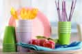 Stacked colorful plastic cups, plates, and utensils with pink tulips and blue napkins on a table.