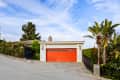 Modern house with a bright orange garage door, surrounded by lush greenery and a sloped driveway.