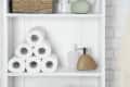 Bathroom shelf with stacked toilet paper rolls, soap dispensers, a wicker basket, and a green decorative stone.