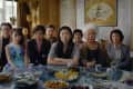 A group of eight people sitting around a table with various dishes, looking intently at the camera.