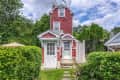 Tall, narrow red house with white trim, surrounded by lush greenery and a lattice fence.