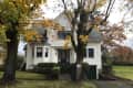 White two-story house with green steps, bay window, and autumn trees in front yard.