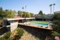 Modern hillside home with large pool, wooden deck, lounge chairs, and surrounding greenery.