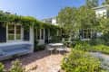 Brick patio with metal table and chairs, surrounded by lush greenery and a vine-covered house exterior.