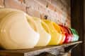 Colorful ceramic pitchers lined up on a rustic wooden shelf against a brick wall.