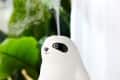Ceramic sloth-shaped humidifier emitting steam, set on a white surface with green plants in the background.