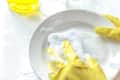 Hands in yellow gloves washing a white plate with a soapy sponge.
