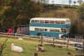 Vintage double-decker bus parked in a rural field with sheep grazing nearby.
