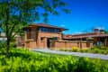 Brick building with large windows, surrounded by lush greenery and colorful flowers under a clear blue sky.