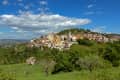 Hilltop village with colorful buildings surrounded by lush greenery under a blue sky with clouds.