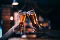 Two people clinking glasses of amber beer in a dimly lit bar.