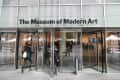 Entrance to The Museum of Modern Art with revolving glass doors and people entering.