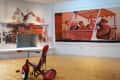 Red tricycle on wooden floor, mural of people in a boat, and painted brick fireplace with abstract art.