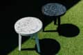 Two terrazzo tables, one white and one black, on green grass, casting shadows.