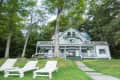 Victorian-style inn with green trim, surrounded by trees, with three white lounge chairs on the lawn.