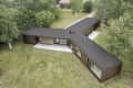 Y-shaped modern house with dark roof, large windows, and wooden exterior, surrounded by lush green trees and grass.