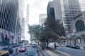 Busy city street with cars, taxis, cyclists, and pedestrians, flanked by tall buildings and American flags.
