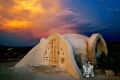 Dome-shaped adobe house with wooden door at sunset, featuring a small robot figure beside it.