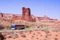 Tour bus and cars on a desert road with red rock formations under a clear blue sky.