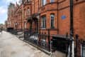 Red brick Victorian terrace houses with ornate black iron railings and a blue plaque on the wall.