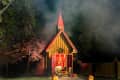 Small wooden chapel with red roof, surrounded by trees and fog, lit pumpkins on porch.