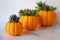 Three orange pumpkin-shaped planters with green succulents on a marble surface.
