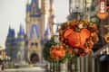 Mickey Mouse pumpkin wreath on a lamppost with a castle in the background, surrounded by autumn leaves.