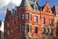 Historic red brick building with turrets and arched windows under a blue sky.
