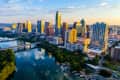 Austin skyline at sunset with skyscrapers reflecting in the river, surrounded by greenery and bridges.