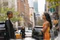 Two women facing each other on a city street, one in a black jacket, the other in a shimmering orange dress.