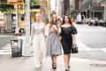 Three women walking on a city street, wearing stylish outfits; one in plaid, one in white, and one in black polka dots.