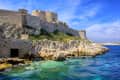 Stone fortress on rocky coastline with turquoise sea under a clear blue sky.
