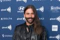 Person with long hair and mustache in a black outfit at a GLAAD event backdrop.