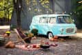Vintage blue van parked outdoors with pumpkins, a deck chair, string lights, and autumn decor.
