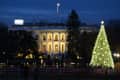 White House illuminated at night with a large decorated Christmas tree in the foreground and people gathered nearby.
