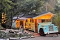Vintage blue bus converted into a cozy cabin with string lights, nestled among trees and surrounded by rustic decor.