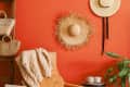 Cozy corner with a tan leather chair, knit blanket, straw hats on orange wall, and a plant.