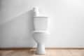 White toilet with two rolls of toilet paper on top, set against a light wooden floor.