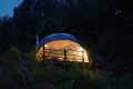 Geodesic dome tent illuminated at night in a forest setting.