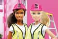 Two dolls in construction gear with pink hard hats and tool belts, standing in front of a pink building.