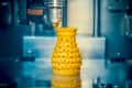 3D printer creating a yellow, textured vase with a spiral design.