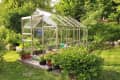 Glass greenhouse surrounded by lush greenery and potted plants on a wooden deck.