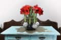 Red amaryllis flowers in a wire basket on a distressed blue table.