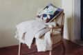 Wooden armchair with a beige throw and a colorful abstract pillow on a terracotta tile floor.